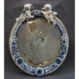 A continental porcelain framed wall mirror with cherub surmount, of oval form,