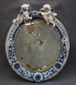 A continental porcelain framed wall mirror with cherub surmount, of oval form,