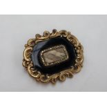 A Victorian mourning brooch, of rectangular shape with a scrolling border to a black ground,