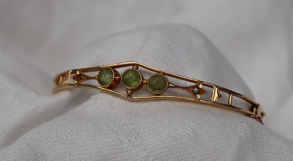 A 14ct yellow gold hinged bangle set with three round cut peridot and a seed pearl, - Image 3 of 3