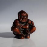 A 19th century Japanese carved wooden netsuke depicting a seated figure with a bag of spirits over