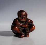 A 19th century Japanese carved wooden netsuke depicting a seated figure with a bag of spirits over