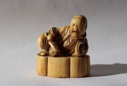 A 19th century Japanese ivory netsuke depicting a reclining sage, holding a fan,