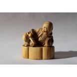 A 19th century Japanese ivory netsuke depicting a reclining sage, holding a fan,