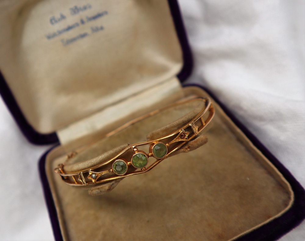 A 14ct yellow gold hinged bangle set with three round cut peridot and a seed pearl,