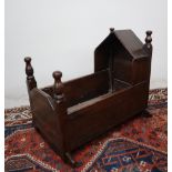 An 18th century oak cot, with a pointed arched top and turned finials, above slat sides on rockers,