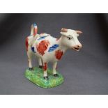 A 19th century pottery cow creamer with iron red and blue patches on a rectangular base,