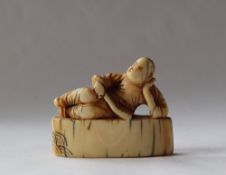 A 19th century Japanese ivory netsuke in the form of a man reclining with a fan in his hand on a