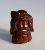 A Japanese carved wooden netsuke depicting Hotei holding a fan,