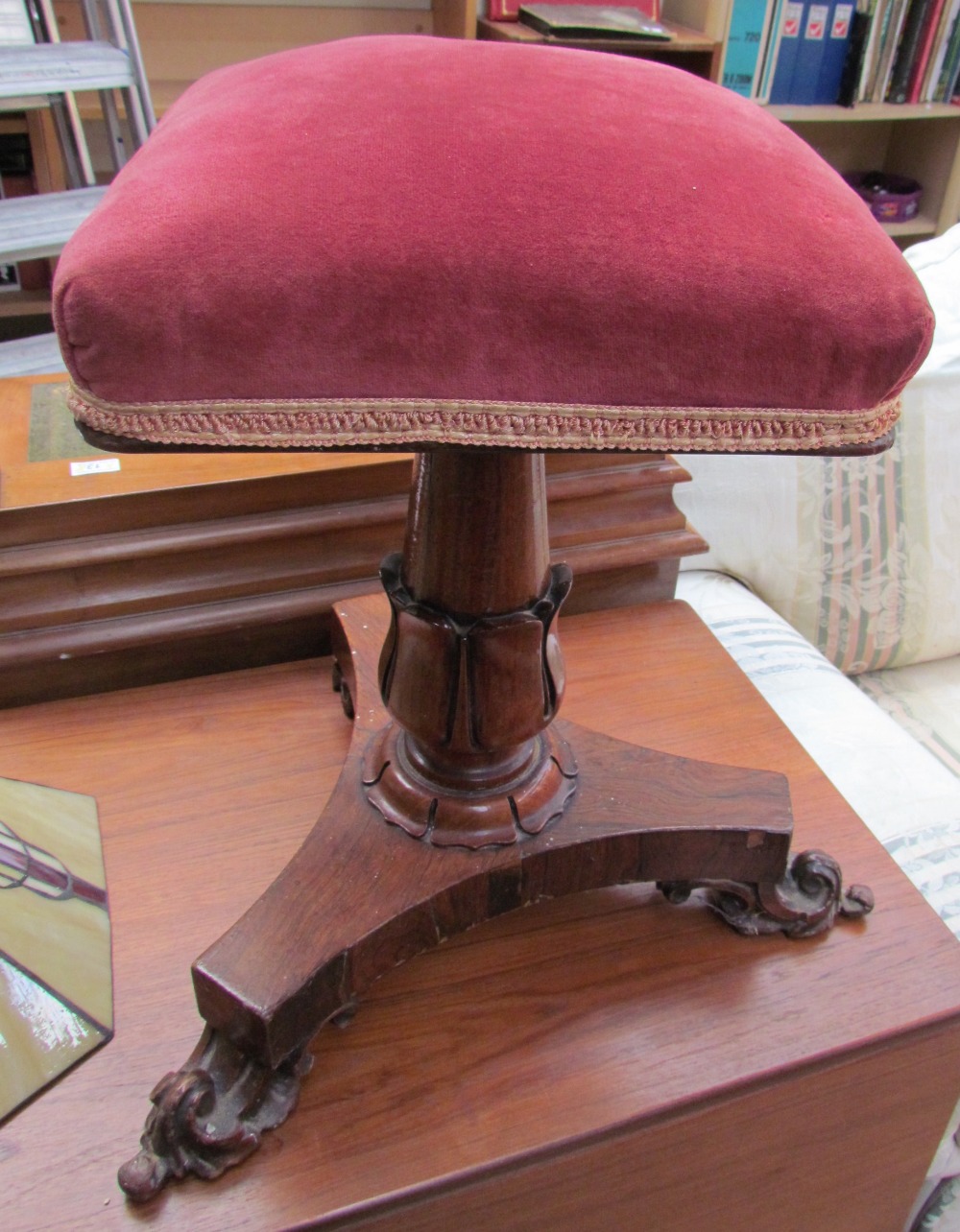 A Victorian rosewood piano stool with a square pad upholstered seat on a leaf carved columns and