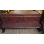 A pine pew, with a panelled back and a solid seat on stiles