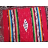 A Mexican rug with a red ground, central geometric panel and multicoloured stripes together with two