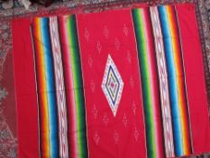 A Mexican rug with a red ground, central geometric panel and multicoloured stripes together with two