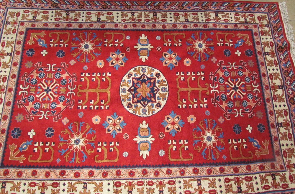 A red ground rug, with a central round medallion and two shaped medallions, with multiple floral