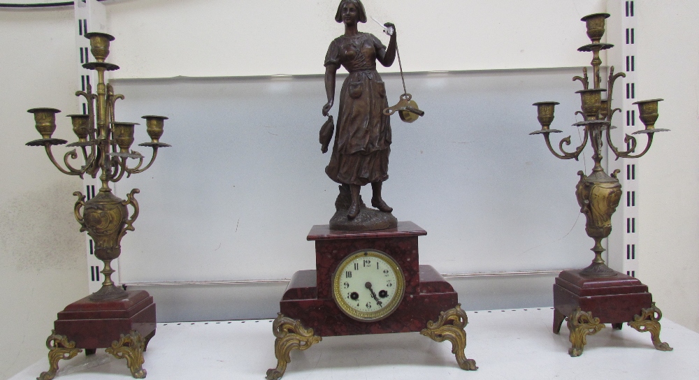 A clock garniture with a fisherwoman surmount, flanked by a pair of candelabra