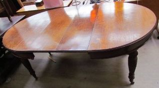 An Edwardian oak extending dining table with two additional leaves on reeded and fluted legs and