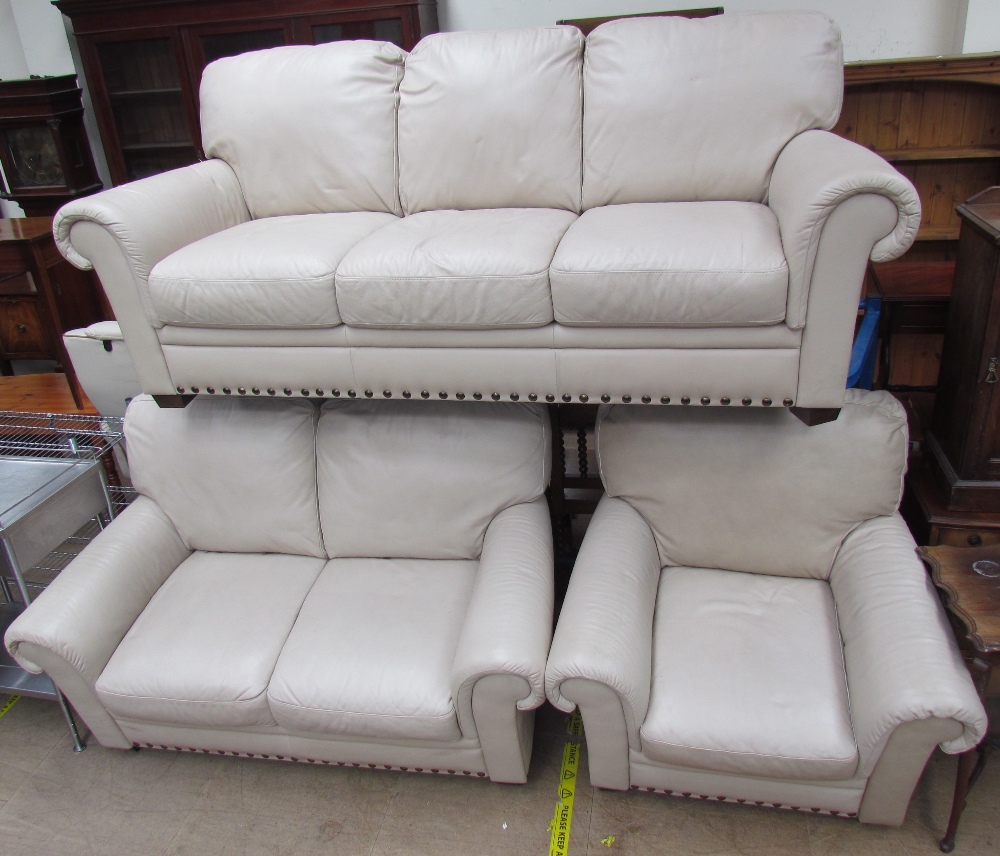 A cream leather three piece suite comprising a three seater settee,