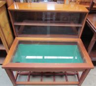 A teak bijouterie table with a hinged glazed top on square legs together with a teak bookcase with