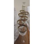 A crystal glass decanter with six matching wine glasses with gilt highlighted rims