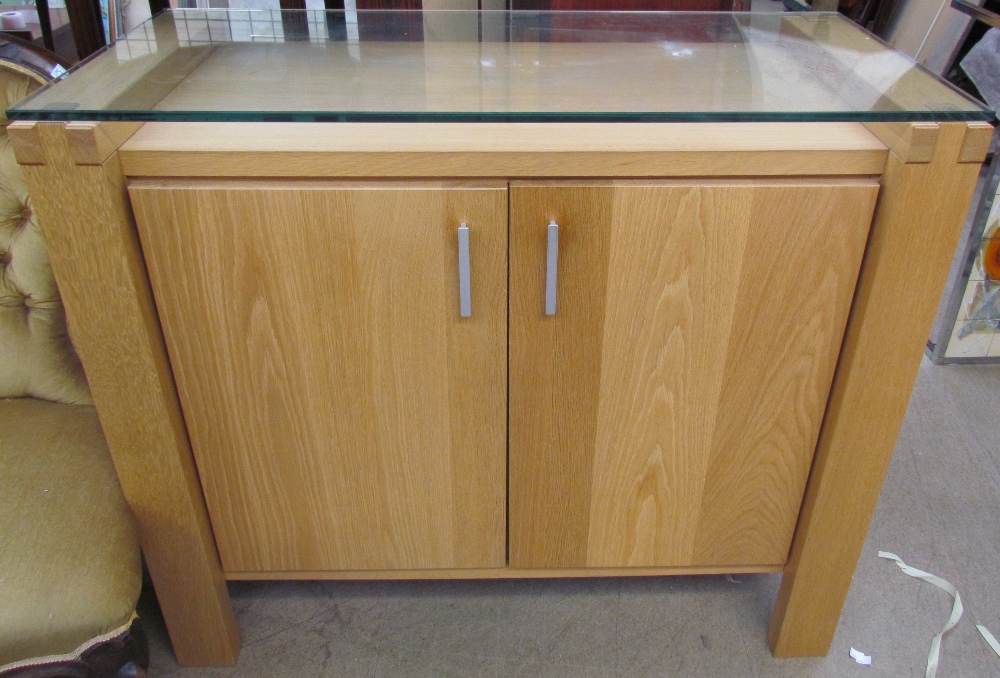A modern oak side cabinet with a glass top and two doors on square legs