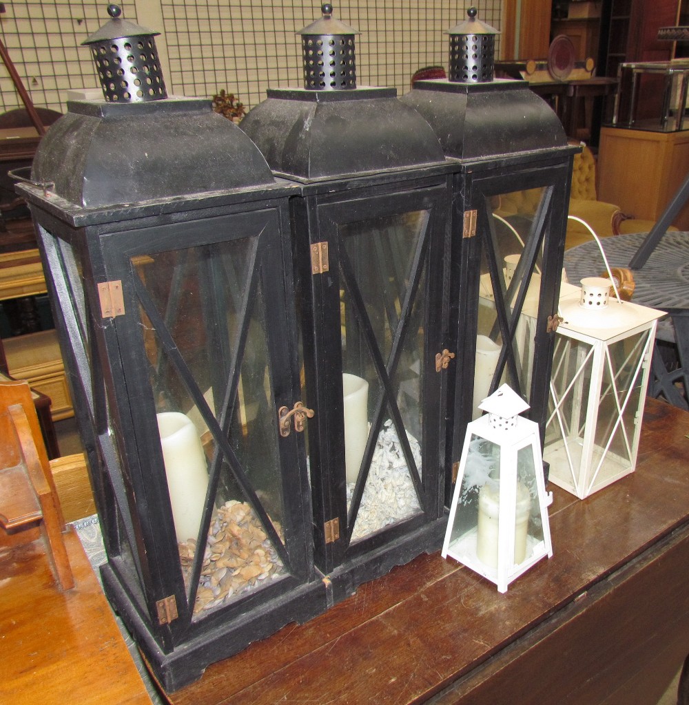 A set of three black painted storm lanterns together with a pair of cream storm lanterns and