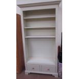 A modern cream painted bookcase with four shelves and a base drawer on bracket feet