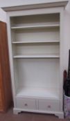 A modern cream painted bookcase with four shelves and a base drawer on bracket feet