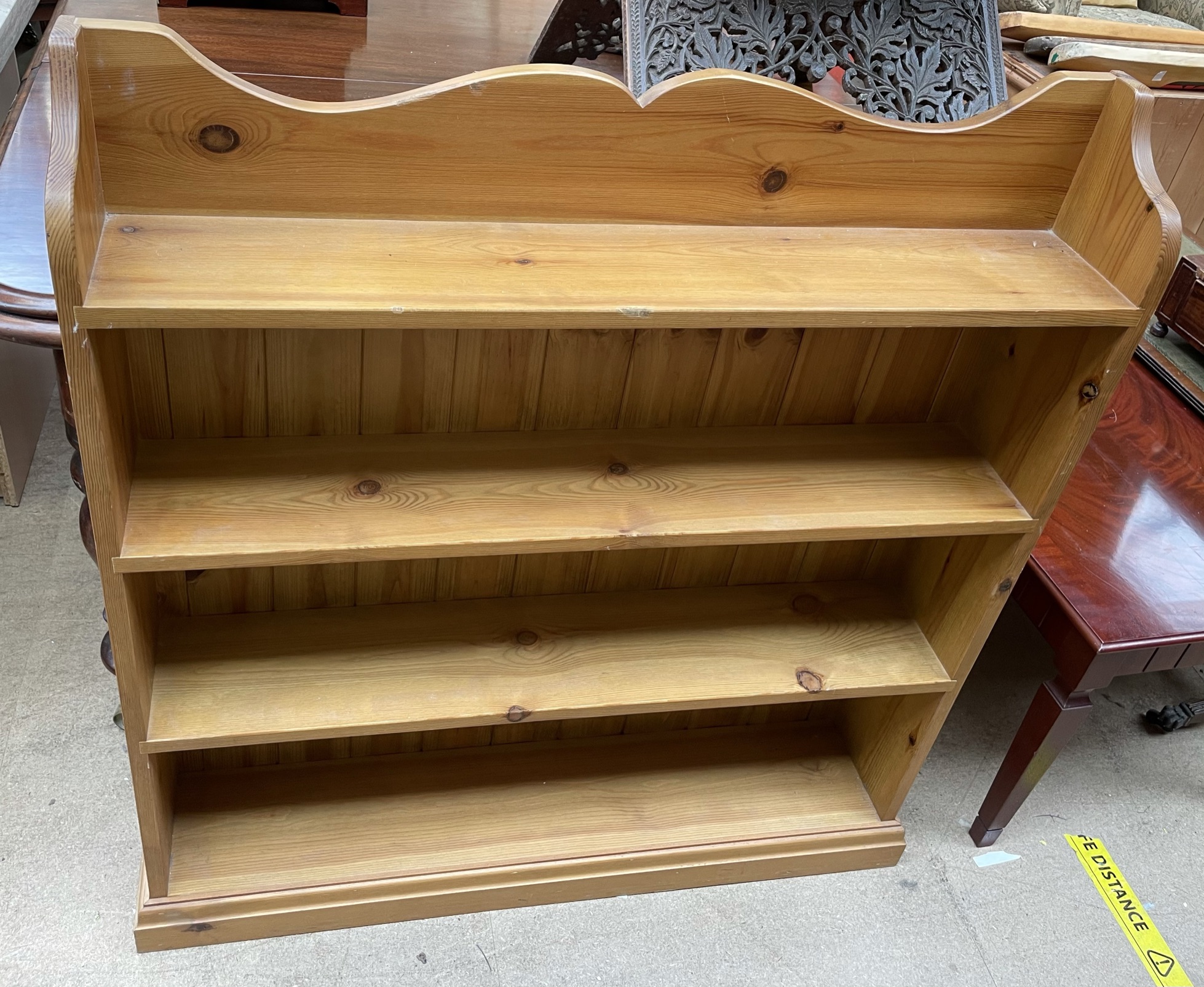A pine bookcase with a shaped back above four shelves