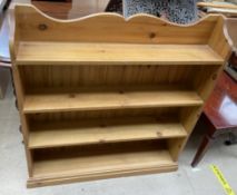 A pine bookcase with a shaped back above four shelves