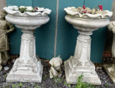 A pair of reconstituted stone planters with flared leaf shaped bowls on a moulded column and square