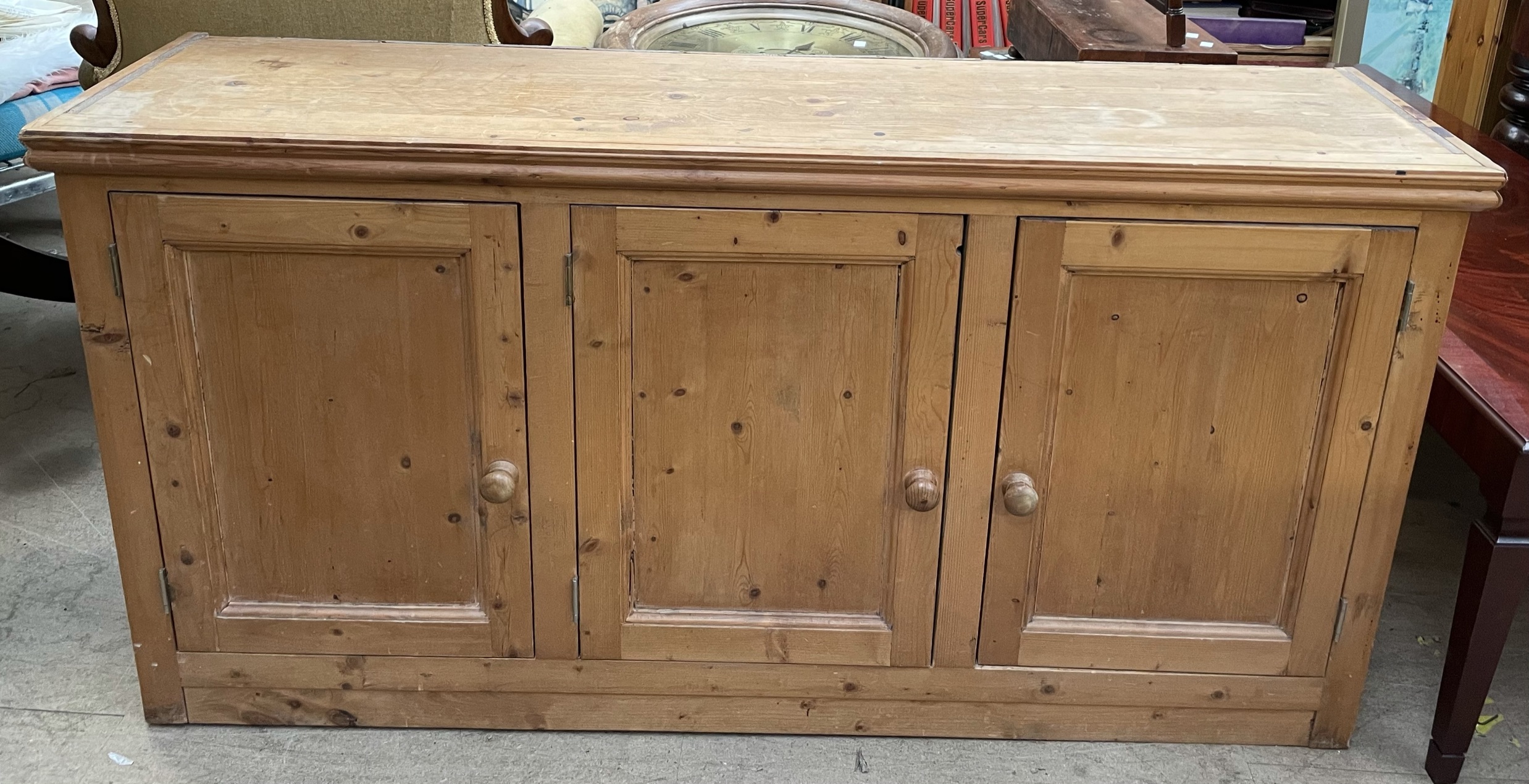 A pine side cabinet with three doors on a plinth base approximately 132cm wide x 34cm deep x 67.