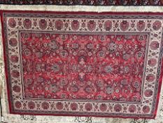 A red ground rug, with interlocking flowerheads and leaves to a cream border and guard stripes,