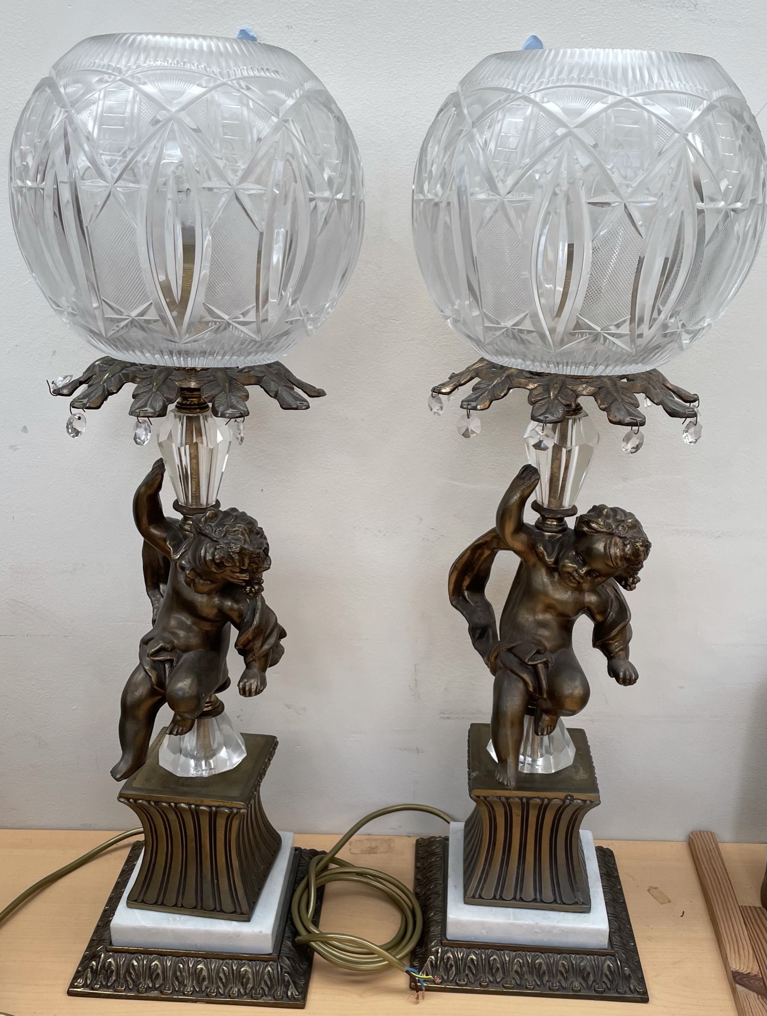 A pair of 20th century table lamps with cut glass globe shades held aloft by cherubs on square