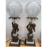 A pair of 20th century table lamps with cut glass globe shades held aloft by cherubs on square