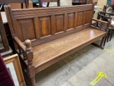 An oak settle with a six panel back and solid seat with turned uprights as part of the arms