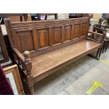 An oak settle with a six panel back and solid seat with turned uprights as part of the arms