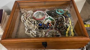 A table top display cabinet containing assorted costume jewellery including necklaces,