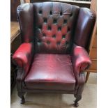 A red leather upholstered wing back chair on cabriole legs