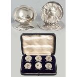 A SET OF SIX GEORGE V SILVER PLACE CARD HOLDERS, BIRMINGHAM 1909, H. MATHEWS, each depicting a