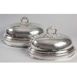A NEAR PAIR OF SILVERPLATE MEAT DOMES, the removable handle embossed with shells, leaves and acorns,