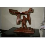A tribal hardwood stool the carved dished seat on a carved bird support and flat platform base.