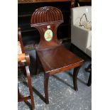 An early 19th century mahogany hall chair, the shaped and low carved back around a central cartouche