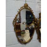 A metal oval framed mirror with scrolling leaf and flower decoration and a modern gilt-framed square