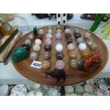 A wooden solitaire board with polished hardwood stones including rose quartz, a malachite figurine