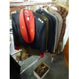 A half rail of clothing including military uniforms and dress jackets, a raincoat, a blazer, etc.