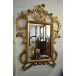 A gold painted wooden framed mirror with ornate scrolling leaf decoration TO BID ON THIS LOT AND FOR