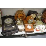 A shelf of clocks including two oak mantel clocks, two metal alarm clocks, two Actim wall clocks, an