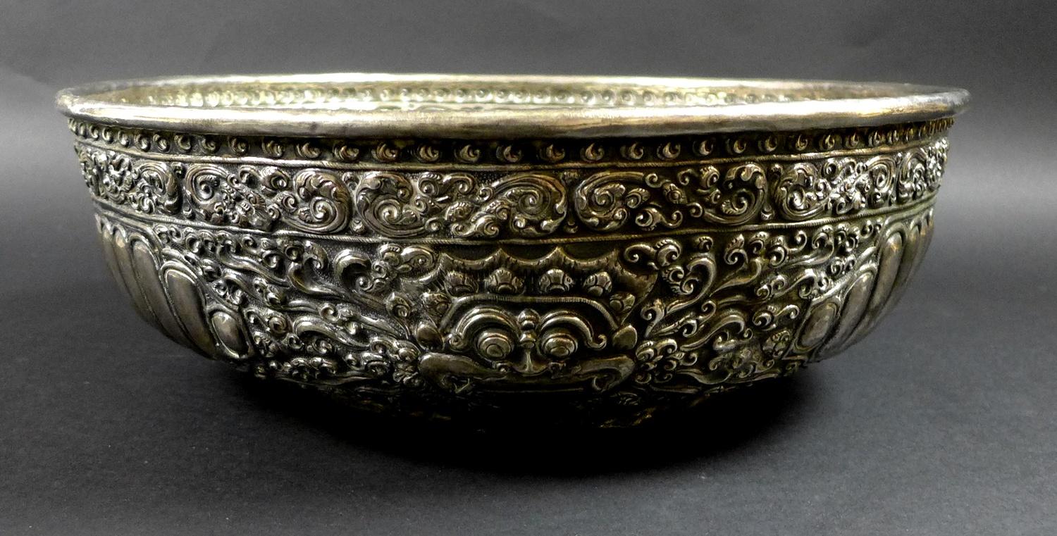 A late 19th century Thai silver large bowl, repousse decorated in relief with three face masks and