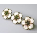 A silver and enamel brooch of apple blossom design, 1930s, composed of three blossoms in a row,
