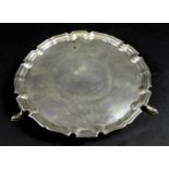 A George V silver waiter tray, of circular form with Chippendale pie crust edge, raised on three
